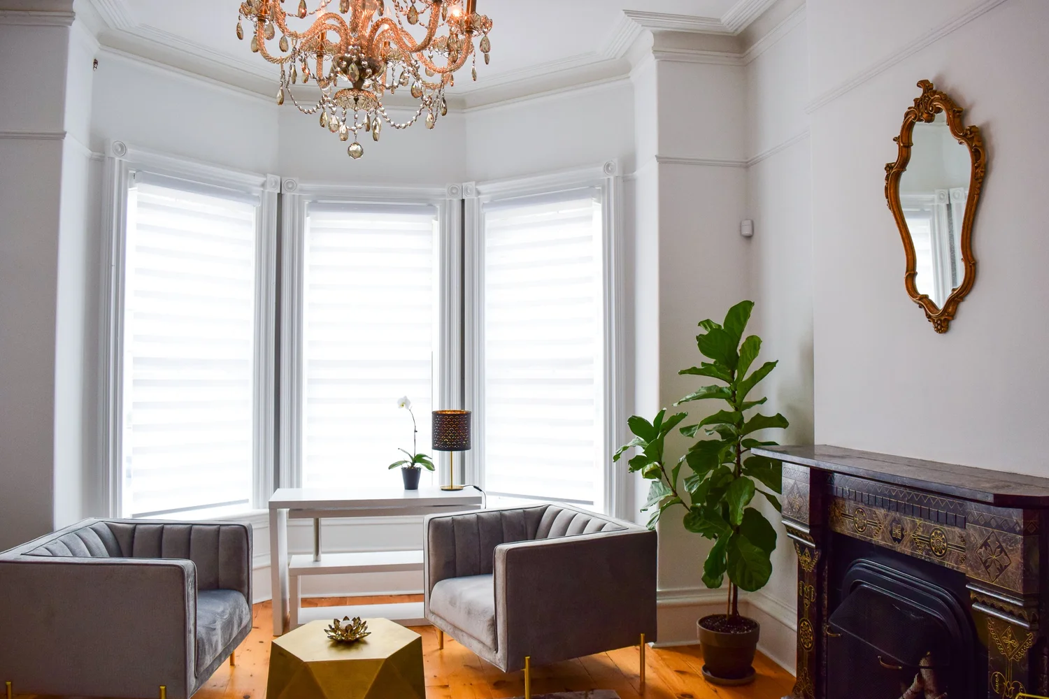 The Chandelier Room at Lotus Counselling Services, a bright bay-window therapy room with two grey velvet armchairs, a copper crystal chandelier, and a fireplace