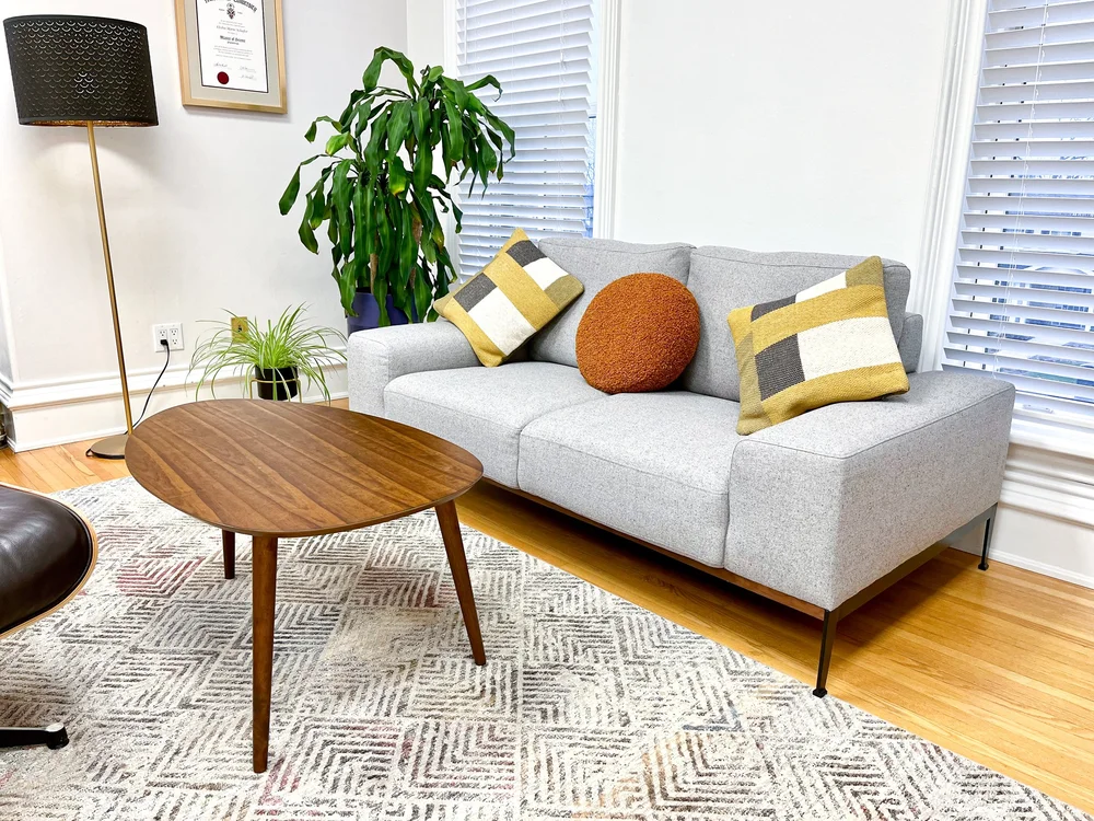 The Marvel Room at Lotus Counselling Services, a cozy sitting space with a grey sofa, accent cushions, a walnut coffee table, and a floor lamp